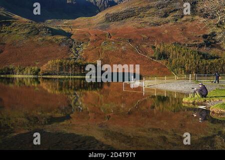 Un fotografo riallinea il suo scatto di riflessi autunnali nel lago Buttermere nel Distretto dei Laghi, Cumbria. Foto Stock