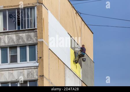 TULA, RUSSIA - 10 OTTOBRE 2020: Operaio di scalatori industriali che applica l'isolamento di polistirolo supplementare sulla parete esterna dell'edificio di appartamenti a nove piani Foto Stock