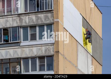 TULA, RUSSIA - 10 OTTOBRE 2020: Operaio di scalatori industriali che applica l'isolamento di polistirolo supplementare sulla parete esterna dell'edificio di appartamenti a nove piani Foto Stock