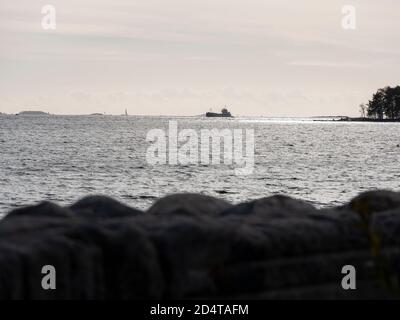 Helsinki/Finlandia - 10 OTTOBRE 2020: Una silhouette di una piccola nave da carico che attraversa l'orizzonte soleggiato. Foto Stock