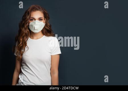 Donna felice che indossa una maschera medica protettiva e una t-shirt bianca sfondo nero Foto Stock