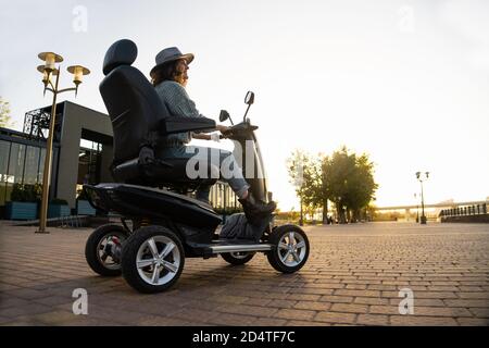 Donna turistica in sella a uno scooter elettrico a quattro ruote su una strada cittadina. Foto Stock