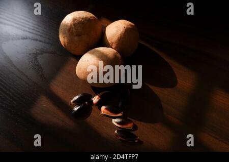 Un colpo vicino di sapota (Chikoo) frutti e semi isolati su sfondo di legno Foto Stock