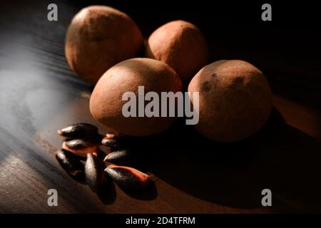 Un colpo vicino di sapota (Chikoo) frutti e semi isolati su sfondo di legno marrone Foto Stock