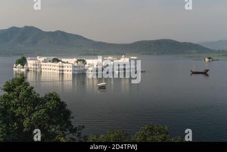 Vista elevata del lago Pichola e Lake Palace hotel con le colline di Aravalli in background su una mattina luminosa a Udaipur, Rajasthan, India. Foto Stock