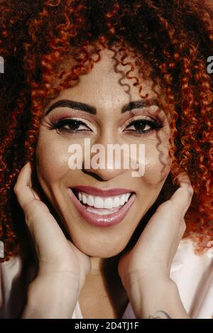 Ritratto di una bella donna afroamericana con un colore rosso arricciato capelli e trucco Foto Stock