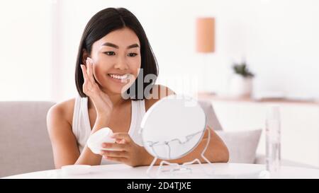 Giovane donna asiatica che applica crema sul viso Foto Stock