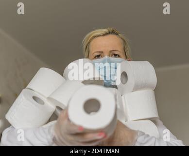 Una donna in maschera medica tiene un'armata di rotoli di carta igienica nelle sue mani. Il hype circa la domanda di carta igienica durante la pandemia globale del coronavirus. Foto Stock