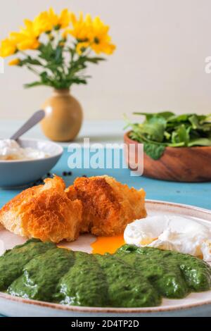 Spinaci freschi e cremosi fatti in casa e uova in camicia con pane tostato. Delizioso brunch o pranzo sano. Sfondo blu tavola di legno, nessuna gente. Foto Stock