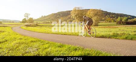 Panorama girato di ciclista su una bici da corsa in scenico paesaggio rurale autunno durante la bella luce del pomeriggio Foto Stock