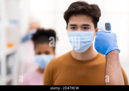 Lavoratore medico che fa lo screening della temperatura per l'uomo asiatico in interni Foto Stock