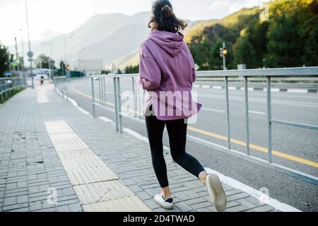 Vista panoramica di una giovane donna che corre su un marciapiede lungo l'autostrada di montagna Foto Stock