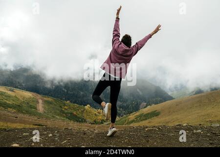 Giovane donna entusiasta godendo la vista in alto sulle montagne nuvolose. Foto Stock