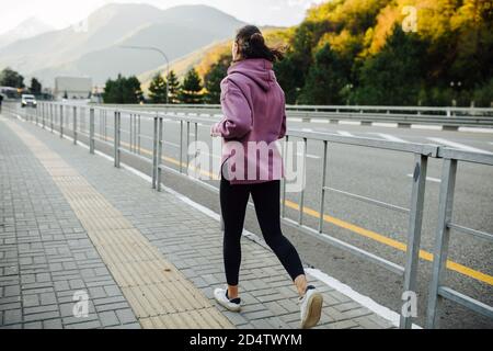 Donna che corre su un marciapiede con barriera in acciaio lungo autostrada di montagna Foto Stock