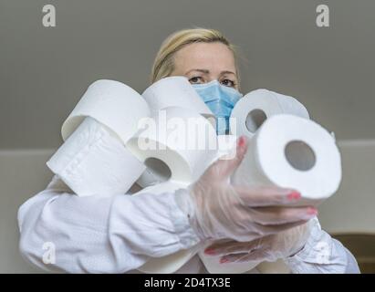 Una donna in maschera medica tiene un'armata di rotoli di carta igienica nelle sue mani. Il hype circa la domanda di carta igienica durante la pandemia globale del coronavirus. Foto Stock