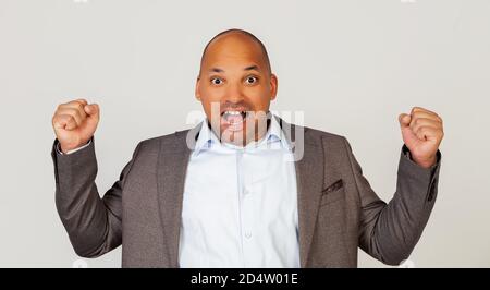 Eccitato giovane uomo d'affari afroamericano gridando forte ed espressivamente gesturando con le sue mani, gioioso uomo positivo aggraffato i suoi pugni, celebrando il suo successo. Operazione riuscita Foto Stock