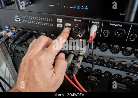 La mano bianca o caucasica preme un pulsante su un pannello di ingresso e uscita di un mixer professionale per la registrazione audio e multimediale. Ingressi e uscite audio Foto Stock