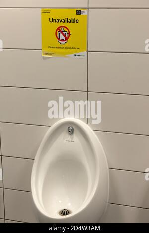 Cartello giallo distanziatore sociale nei servizi igienici per uomini o uomini WC pubblico e orinatoio non in uso a causa della pandemia di COVID 19 all'aeroporto di Dublino, Irlanda, Europa Foto Stock