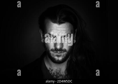 L'uomo con i capelli lunghi guarda seriamente e determinato al fotocamera su un'immagine in bianco e nero Foto Stock