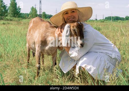 Una donna in un cappello di paglia abbraccia una capra anglo-nubiana. Un contadino con una capra nubiana. Foto Stock