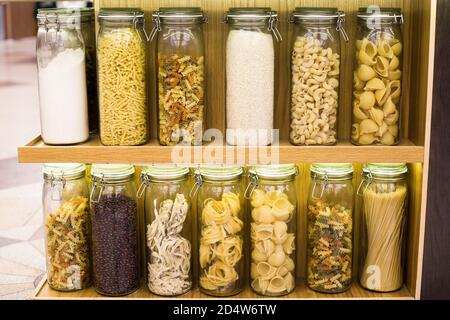 Diversi tipi di pasta cruda spaghetti, fettuccine, pappardelle, fusilli, cavatappi, pipe rigate, gemelli e cereali, riso sono immagazzinati in chiuso Foto Stock