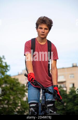 Un giovane in una t-shirt rossa si pone in piedi su una bicicletta . Foto Stock