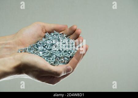 Bulloni nelle mani di un uomo. Viti e denti. Attrezzi per il fissaggio e la riparazione. Bulloni in acciaio inox. Dispositivi di fissaggio in metallo galvanizzato. Pila di viti metalliche chiusa Foto Stock