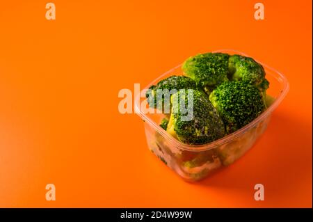 Verdure surgelate broccoli in un vassoio di plastica su sfondo arancione, fuoco selettivo, diete concettuali e alimentazione sana con spazio di copia primo piano Foto Stock