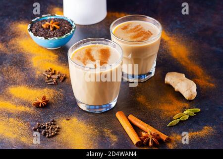 Caraffa per tè e latte Masala chai su sfondo nero. Due bicchieri di tè masala e spezie sparse. Vista dall'alto Foto Stock