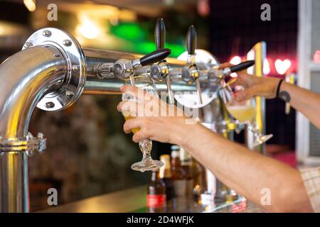 Primo piano delle mani della persona che riempiono due tazze di birra alla volta in un bar. Messa a fuoco selettiva. Foto Stock