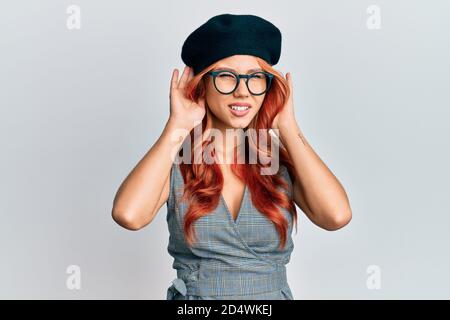 Giovane donna rossa indossando moda francese look con beretto cercando di sentire entrambe le mani sul gesto dell'orecchio, curioso per pettegolezzi. Problema uditivo, sordi Foto Stock