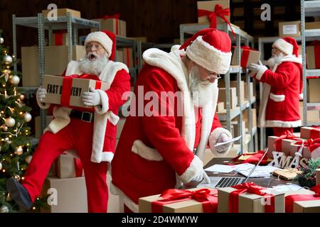 Molte clausole di Babbo Natale che imballano presenta le scatole del regalo che preparano la consegna rapida di Natale. Foto Stock