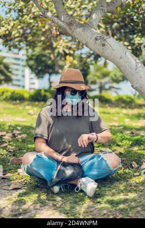 Donna guarda il suo orologio all'aperto e si protegge con una maschera medica. Nuovo normale Foto Stock