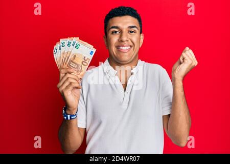 Giovane arabo che detiene 50 banconote in euro gridando orgoglioso, celebrando la vittoria e il successo molto eccitato con Raised ARM Foto Stock