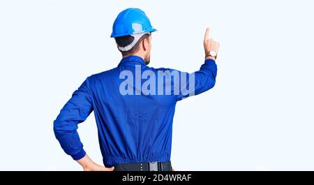 Giovane bell'uomo che indossa uniforme operaio e hardhat pensiero all'indietro circa il dubbio con la mano sulla testa Foto Stock