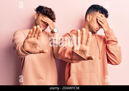 Giovane coppia gay che indossa abiti casual che coprono gli occhi con le mani e che fa gesto di stop con espressione triste e paura. Imbarazzato e negativo concetto Foto Stock