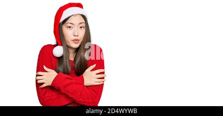 Giovane donna cinese che indossa cappello di natale scuotendo e congelando per freddo invernale con espressione triste e shock sul viso Foto Stock