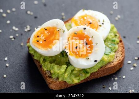 Tostare con avocado e uovo guarnito con semi di sesamo bianchi e neri. Spuntini sani o cibi per la colazione Foto Stock