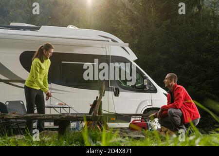 Auto ricreativa a casa automobilistica tempo di vacanza viaggio su strada. Romantico campeggio estivo RV Van Camper Wilderness. Coppia caucasica divertirsi accanto a Campfire Foto Stock