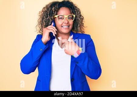 Giovane afroamericano più taglia donna che indossa occhiali che hanno conversazione parlare sullo smartphone sorridendo felice indicando con la mano e. dito Foto Stock