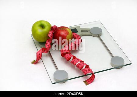 Due mele fresche verdi e rosse con nastro di misurazione su pavimento in vetro bilancia sfondo bianco Foto Stock