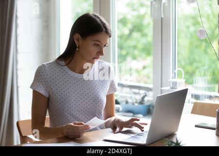 Giovane donna concentrata che paga le fatture di utilità in linea. Foto Stock