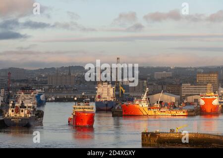 Il sole della mattina presto mette in evidenza le navi di supporto e le barche di rifornimento Attraccato nel porto di Aberdeen sulla costa nord-orientale di Scozia Foto Stock