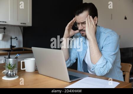 Un giovane overlavored che soffre di mal di testa in ufficio domestico. Foto Stock