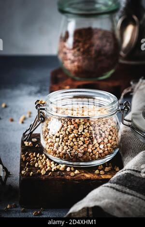 Groat di grano saraceno verde senza cottura in vaso di vetro, cibo vegetariano sano su tavolo da cucina grigio, spazio copia, fuoco selettivo Foto Stock