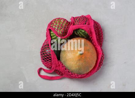 Varie zucche colorate e piccoli cocomeri in sacchetto di maglia colore fucsia su sfondo chiaro, concetto Zero Waste, Vista dall'alto. Foto Stock