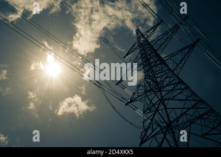 Un pilone elettrico si erge alto nel caldo sole estivo con alcune nuvole wisy. Concetto di energia solare. Foto Stock