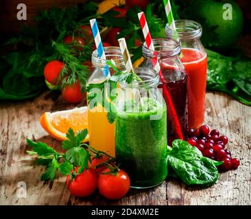 Miscela di succhi di frutta e verdura sani in piccole bottiglie con cannucce a righe colorate, fondo di legno vecchio, fuoco selettivo Foto Stock