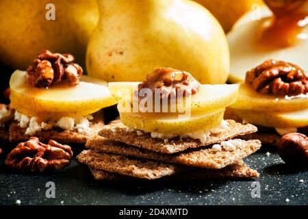 Antipasto da pane scuro croccante, formaggio di cottage, noci e pere con miele, sfondo scuro, fuoco selettivo Foto Stock