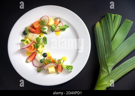 Pesce rosso, verdure e Macedonia di frutta su un piatto bianco. Involtini di filetto di pesce, rafano, involtini di zucchine, micrograni, spicchi di fragola, cubetti di mango, succo di frutta Foto Stock